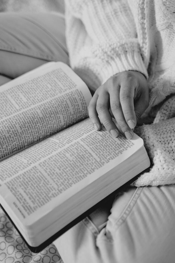 Black and white image of a person reading, emphasizing hands and text.